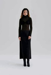 Melna garām piedurknēm adīta augšdaļa ar augstu apkakli, saskaņota ar garu melnu svārku. Teksturēta auduma, augšdaļa pieguloša, apakšdaļa plūstoša.