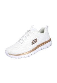 Zapatilla deportiva blanca con cordones blancos, parte superior de malla transpirable, tira de acento dorada y logo "S" dorado en el lateral, suela deportiva con patrón de agarre.