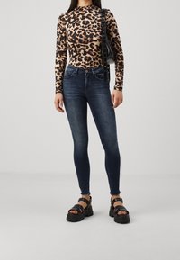 Camiseta de manga larga con estampado de leopardo combinada con jeans ajustados de color azul oscuro y sandalias negras de plataforma. El conjunto presenta una silueta estilizada y telas texturizadas.
