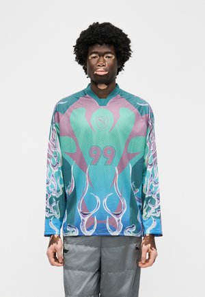 Vitiligohaigusega inimene kannab pika varrukaga mitmevärvilist spordisärki numbriga 99 ja varrukatel abstraktsete leegimustritega.