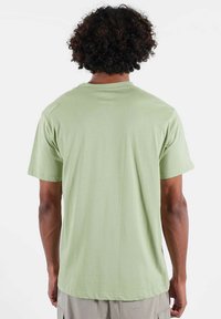 T-shirt vert clair à manches courtes, texture douce, encolure arrondie et coupe ample, avec un design simple et épuré.