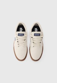 Beige kangast Etnies tennisjalanõusid pruunide kummitaldade ja valgete paeltega, nähtud pealtpoolt valgel taustal.