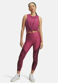 Fitted purple athletic top with knotted front and matching leggings featuring dark patterned accents. Paired with white athletic shoes.