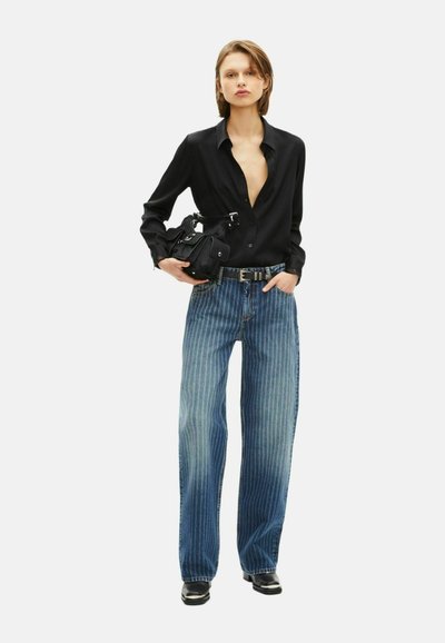 Czarna koszula z guzikami i niskim dekoltem, zestawiona z jasno niebieskimi spodniami w paski. Dodatki obejmują małą czarną torebkę i ciemne obuwie.