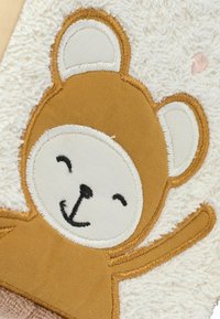 Brown and white bear applique with embroidered features on a fluffy, cream-textured background. Soft, plush material with minimal accents.
