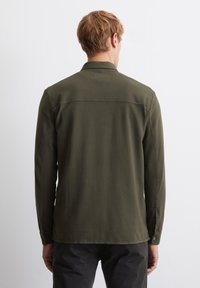 Olive green shirt with long sleeves, buttoned cuffs, and a plain texture, featuring a yoke design across the shoulders.