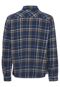 Camisa de cuadros azul marino con líneas amarillas y azul claro, de mangas largas, con puños abotonados y cuello estándar. Tejido texturizado y corte relajado.