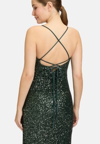 Grünes Paillettenkleid mit einer figurschmeichelnden Silhouette, das über überkreuzte Träger und ein gebundenes Rücken-Design verfügt. Der Stoff glänzt mit einer strukturierten Oberfläche.
