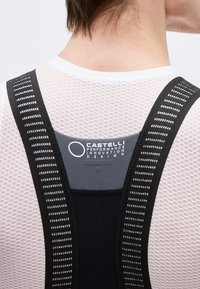 Vue arrière d'une personne portant un maillot de cyclisme en maille blanche et des bretelles de cuissard noires Castelli avec un logo sur le haut du dos.