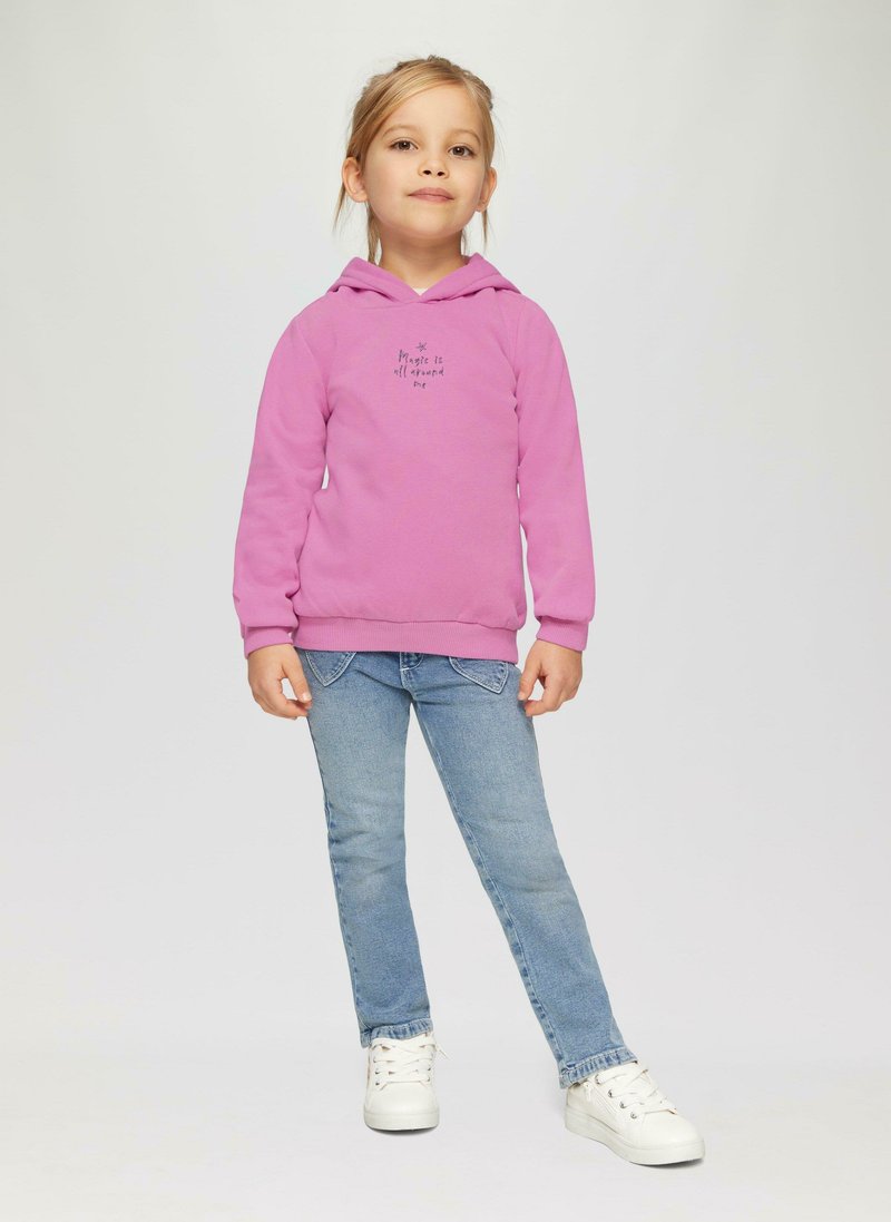 Roze hoodie met een print aan de voorkant en een trekkoordcapuchon, gecombineerd met blauwe jeans en witte sneakers, voor een effen lichte achtergrond.