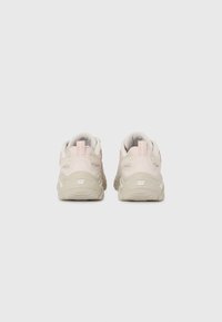 Beige and light pink sporty sneakers with textured surfaces, a padded collar, and rubber soles featuring a distinctive logo on the heel.