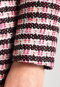 Geweven roze, zwarte en witte tweedstof met een textuureinde; heeft een gestreept patroon met kleurrijke draden door het geheel.