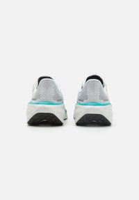 Un paio di scarpe da corsa bianche e turchesi con suole nere viste da dietro su uno sfondo bianco.