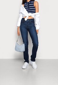 Navy striped sleeveless polo, white wrap shirt, dark blue skinny jeans, white sneakers, and a light blue handbag with chain strap.