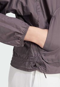 Lätt, lila jacka med elastiska manschetter och rynkad nederkant. Har en sidoficka och dragkedjeslutning för praktisk användning.