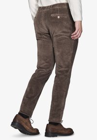 Braune Cordhosen im Slim-Fit mit senkrechter Rippung, zwei Gesäßtaschen und einem Knopfdetail. Präsentiert mit braunen Schuhen.