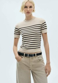 Beige short-sleeve top with horizontal black stripes, round neck, and ribbed hem. Paired with light-colored jeans and a black belt.