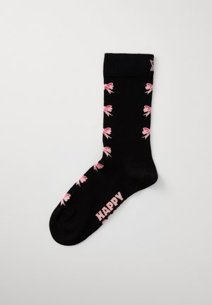 Chaussette noire avec des motifs de nœuds roses sur le côté et le texte "HAPPY" en rose en bas. Fabriquée dans un matériau doux et extensible.