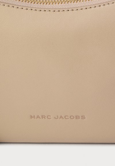 Accessoire en cuir beige Marc Jacobs avec coutures visibles et nom de la marque embossé près du centre en bas.