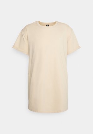 T-shirt beige à manches courtes avec col rond et petit logo sur le côté gauche de la poitrine, présenté sur un fond clair uni.