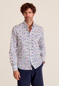 Witte shirt met een kleurrijk bloemenpatroon, vastgemaakt met een gespreid kraag. Gecombineerd met donkerblauwe shorts, van een gestructureerde stof met een luchtig gevoel.