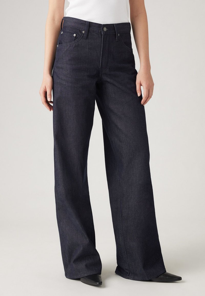 Φαρδιές ντενιμ παντελόνες σκούρου χρώματος με ελαφρώς υφασμάτινη υφή, διαθέτουν μπροστινές τσέπες, κλείσιμο με κουμπί και πέντε θηλιές ζώνης.