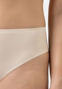 Beige saumattomat alushousut, joissa on sileä pinta ja leveä vyötärönauha. Ne esittelevät minimalistista muotoilua ja istuvaa leikkausta lanteilla.