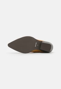 Sula i mörkbrun gummi med en spetsig form. Övermaterialet är ljusbrunt mocka med söm-detaler. Tillverkad i Italien.