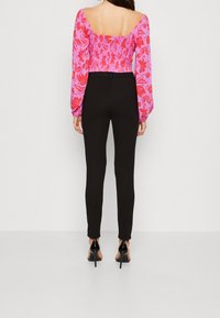 Haut à manches longues imprimé floral rose avec dos froncé, associé à un legging noir moulant et des talons noirs à lanières.