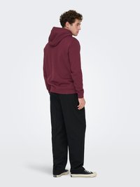 Maroon hoodie, cotton blend, with a drawstring hood. Paired with black, loose-fit trousers and black sneakers. Textured fabric, casual design.