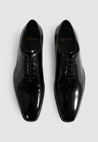 Scarpe stringate in pelle nera lucida con design a punta. Presentano una finitura liscia e un logo dorato sulla soletta.