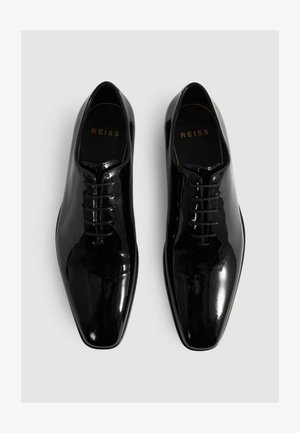 Zapatos de cuero negro pulido con cordones y diseño de punta. Presentan un acabado suave y un logo dorado en la plantilla.