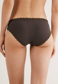 Bruine katoenen hipsteronderbroek met een scalloped kanten rand langs de tailleband en beenopeningen, met een gladde, matte textuur.