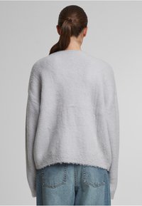 Helles graues, oversize Sweatshirt mit strukturiertem Finish, weitem Rundhalsausschnitt und geripptem Saum. Kombiniert mit hoch taillierten, lockeren blauen Jeans.
