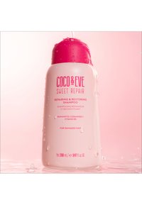 Coco & Eve Sweet Repair Shampoo in een witte fles met een roze dop. De tekst bevat productdetails in het roze. De fles is nat, wat versheid aangeeft.