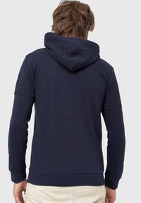 Marineblauwe hoodie met een gestructureerde, gevoerde capuchon en schouderpanelen. Beschikt over een kangoeroezak en ribgebreide manchetten en onderzoom. Gemaakt van gladde katoenstof.