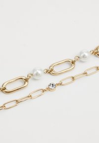 Duas pulseiras de corrente de ouro, uma com grandes elos ovais e pérolas, e a outra com elos menores e uma pedra preciosa redonda e clara.