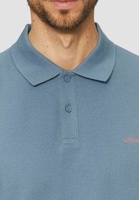 Hellblaues Poloshirt aus strukturiertem Stoff mit klassischem Kragen und zwei Knöpfen. Kleines, rosa gesticktes Logo auf der Brust.