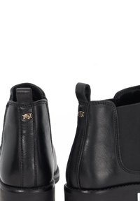 Black leather ankle boots with elastic side panels and a loop tab. Features a small gold logo detail near the heel. Smooth texture.