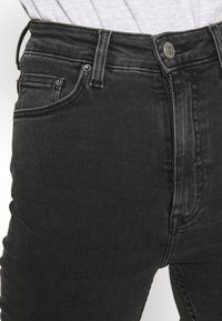 Černé džíny z denimu s vysokým pasem, s předními kapsami a zapínáním na knoflík. Tkanina má mírně texturovaný povrch.
