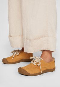 Scarpe stringate in suede marrone con suola in gomma testurizzata e punta rinforzata, abbinate a pantaloni corti in lino beige chiaro.