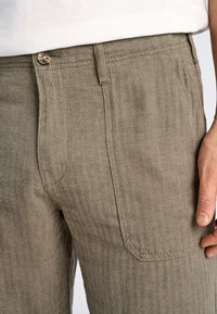 Olijfgroene broeken met een visgraatpatroon, met een knoopsluiting en zijzakken; gestructureerde stof met een lichte glans.
