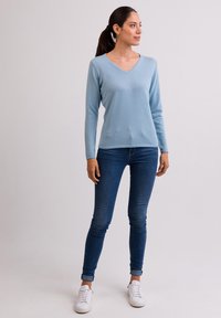 Vaaleansininen v-pääaukko villapaita pehmeästä kankaasta, yhdistettynä slim fit tummiin farkkuihin. Valkoiset tennarit täydentävät asua.