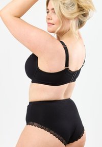 Svart lingerie-set som består av en behå med justerbara band och spetsdetaljer, samt högmidjade trosor med böljande kanter.