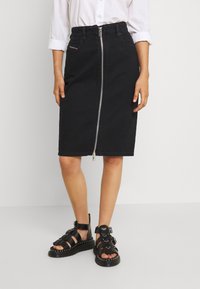 Svart denim midi kjol med silvrig dragkedja, figurnära passform och subtila sömdetaljer; matchad med svarta sandaler med remmar.