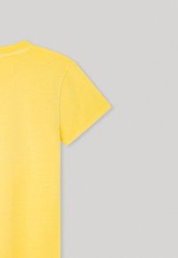 Camiseta amarilla de manga corta, hecha de tela suave, con cuello redondo y textura lisa, con una forma ligeramente ajustada.