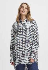 Camisa abotonada con un patrón de cuadrícula en azul, blanco y naranja. Mangas largas, corte relajado y dobladillo curvado. Tejido ligero y superficie texturizada.