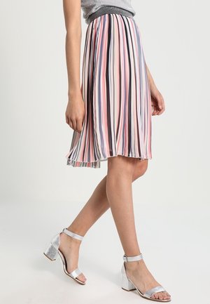 Mujer vistiendo una falda plisada hasta la rodilla con rayas verticales en rosa, blanco, negro y azul, combinada con sandalias plateadas de tacón ancho.