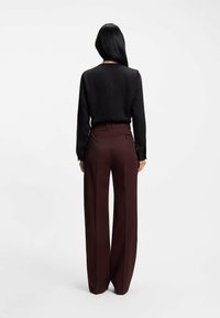 Blusa nera a maniche lunghe abbinata a pantaloni larghi bordeaux. La blusa presenta un semplice design sul retro; i pantaloni hanno una tasca posteriore singola.