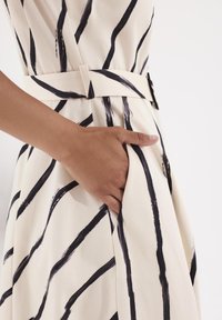 Sukienka z paskiem w kremowym materiale z wyrazistymi czarnymi wzorami w pędzlu, z boczną kieszenią i płynnym krojem.